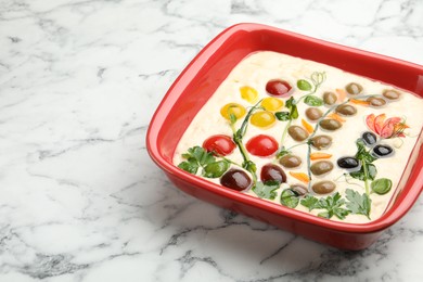 Photo of Raw focaccia with vegetables and olives in baking dish on white marble table, closeup