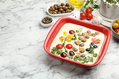 Photo of Raw focaccia with vegetables, olives and spices on white marble table, closeup. Space for text