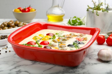 Photo of Raw focaccia with vegetables, olives and spices on white marble table, closeup