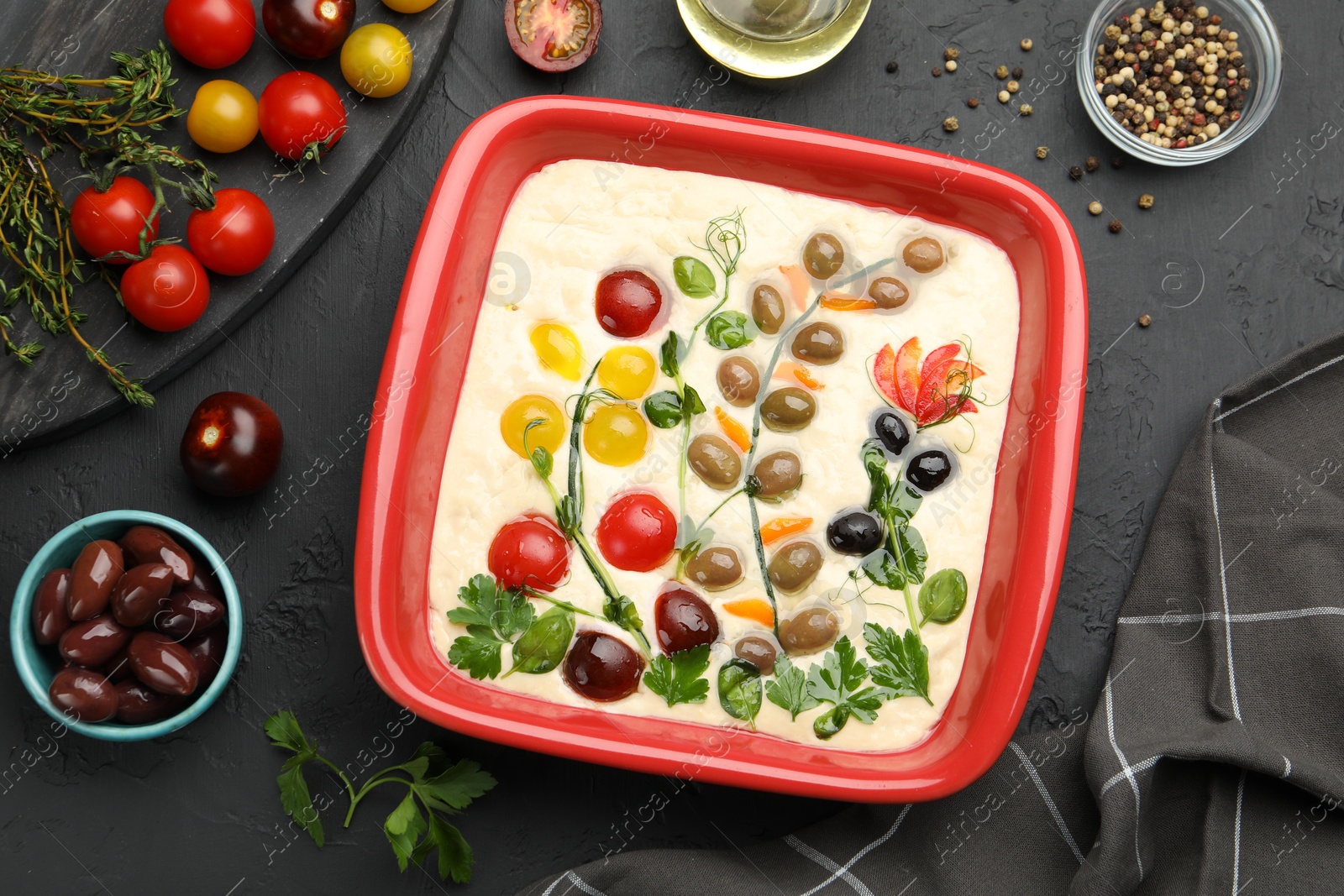 Raw focaccia with vegetables, olives and spices on black table, flat lay Photo of Raw focaccia with vegetables, olives and spices on black table, flat lay