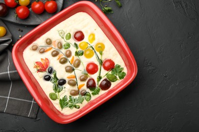 Photo of Raw focaccia with vegetables, olives and spices on black table, flat lay. Space for text