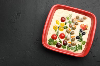 Photo of Raw focaccia with vegetables and olives in baking dish on black table, top view. Space for text