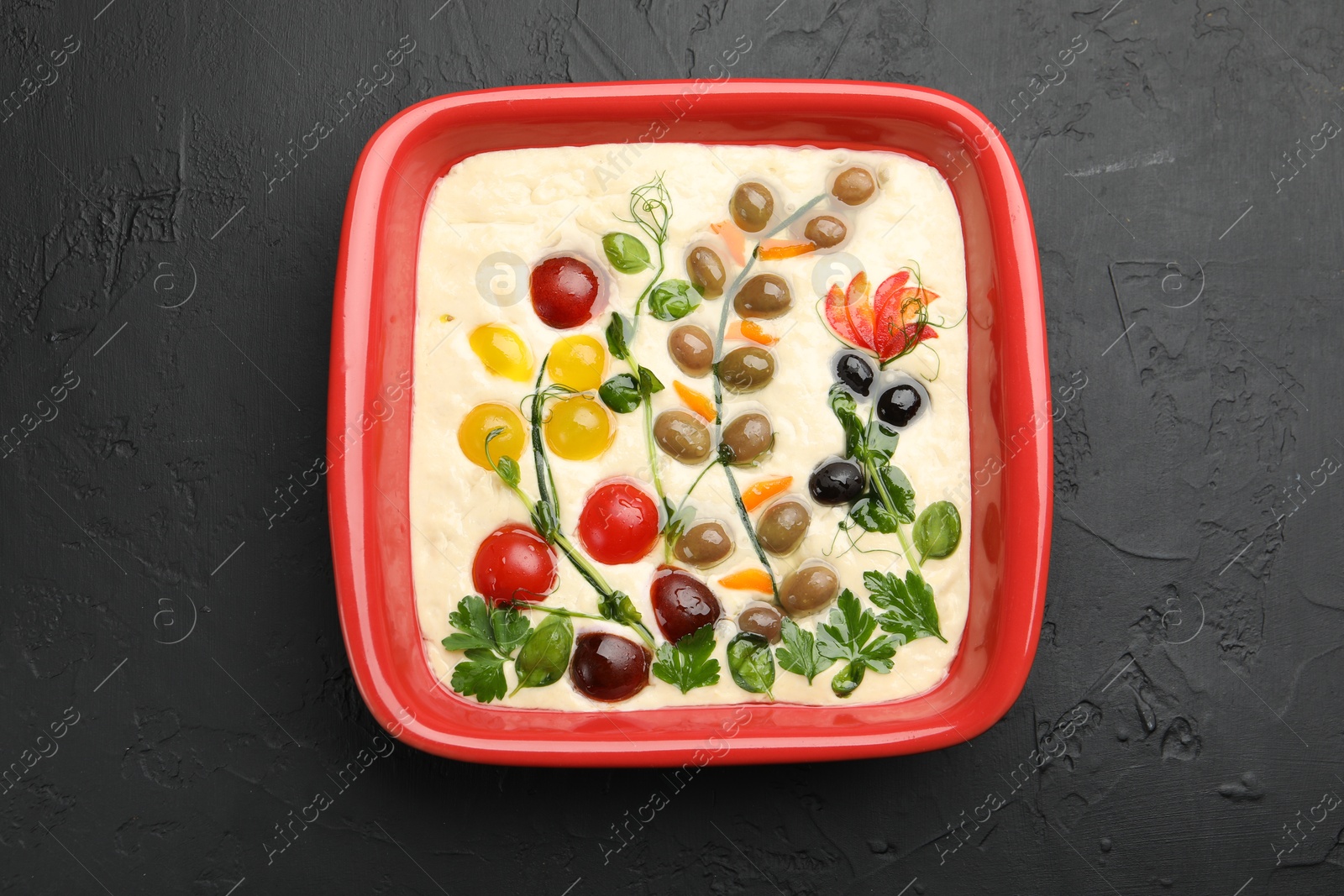 Raw focaccia with vegetables and olives in baking dish on black table, top view Photo of Raw focaccia with vegetables and olives in baking dish on black table, top view