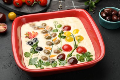 Photo of Raw focaccia with vegetables, olives and spices on black table, closeup