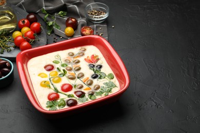 Photo of Raw focaccia with vegetables, olives and spices on black table, closeup