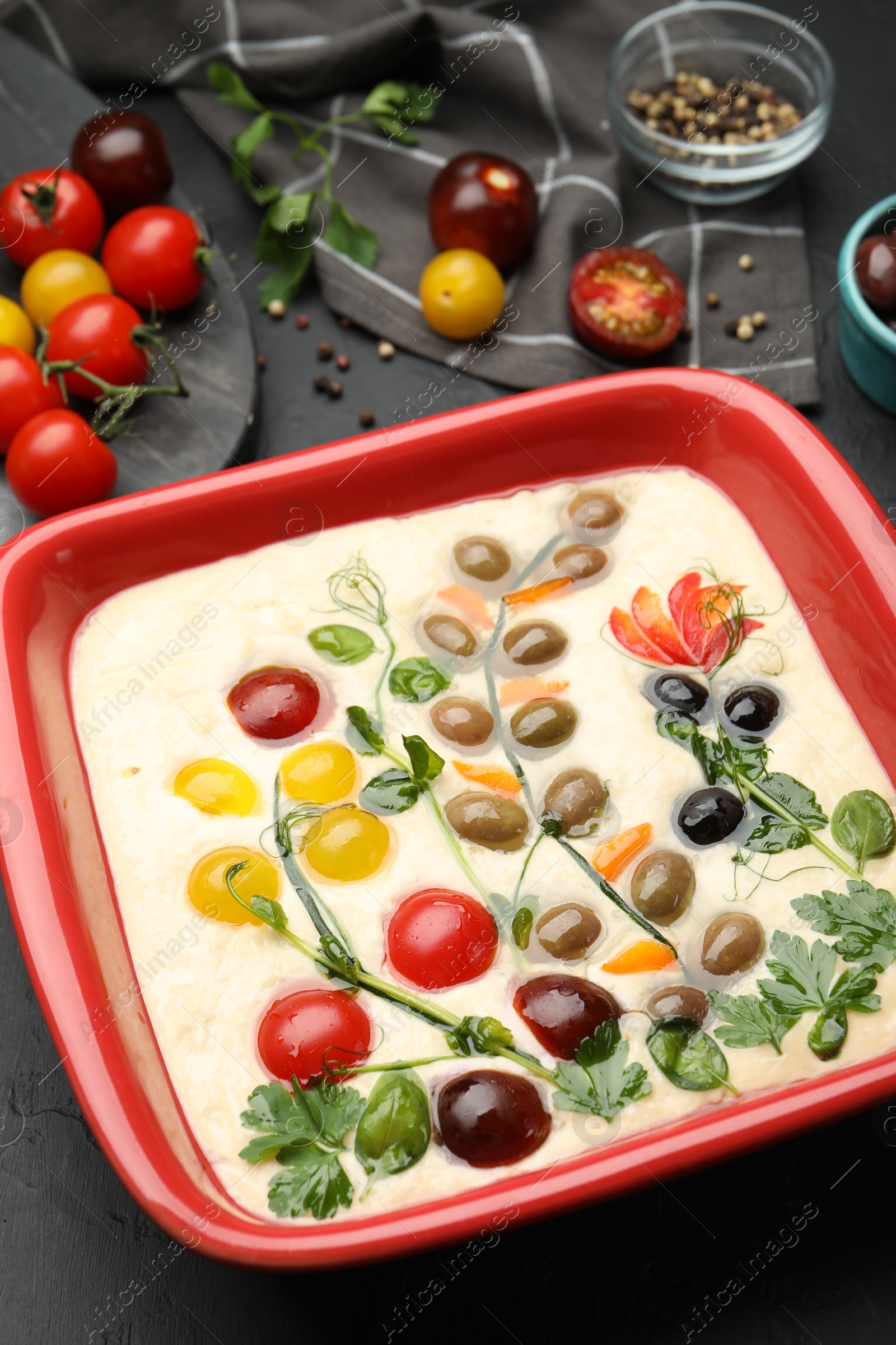 Raw focaccia with vegetables, olives and spices on black table, closeup Photo of Raw focaccia with vegetables, olives and spices on black table, closeup