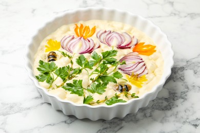 Photo of Raw focaccia with vegetables and olives in baking dish on white marble table, closeup