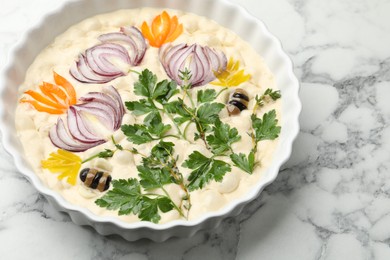 Photo of Raw focaccia with vegetables and olives in baking dish on white marble table, above view