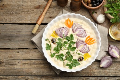 Photo of Raw focaccia with vegetables, olives, spices and brush on wooden table, flat lay. Space for text