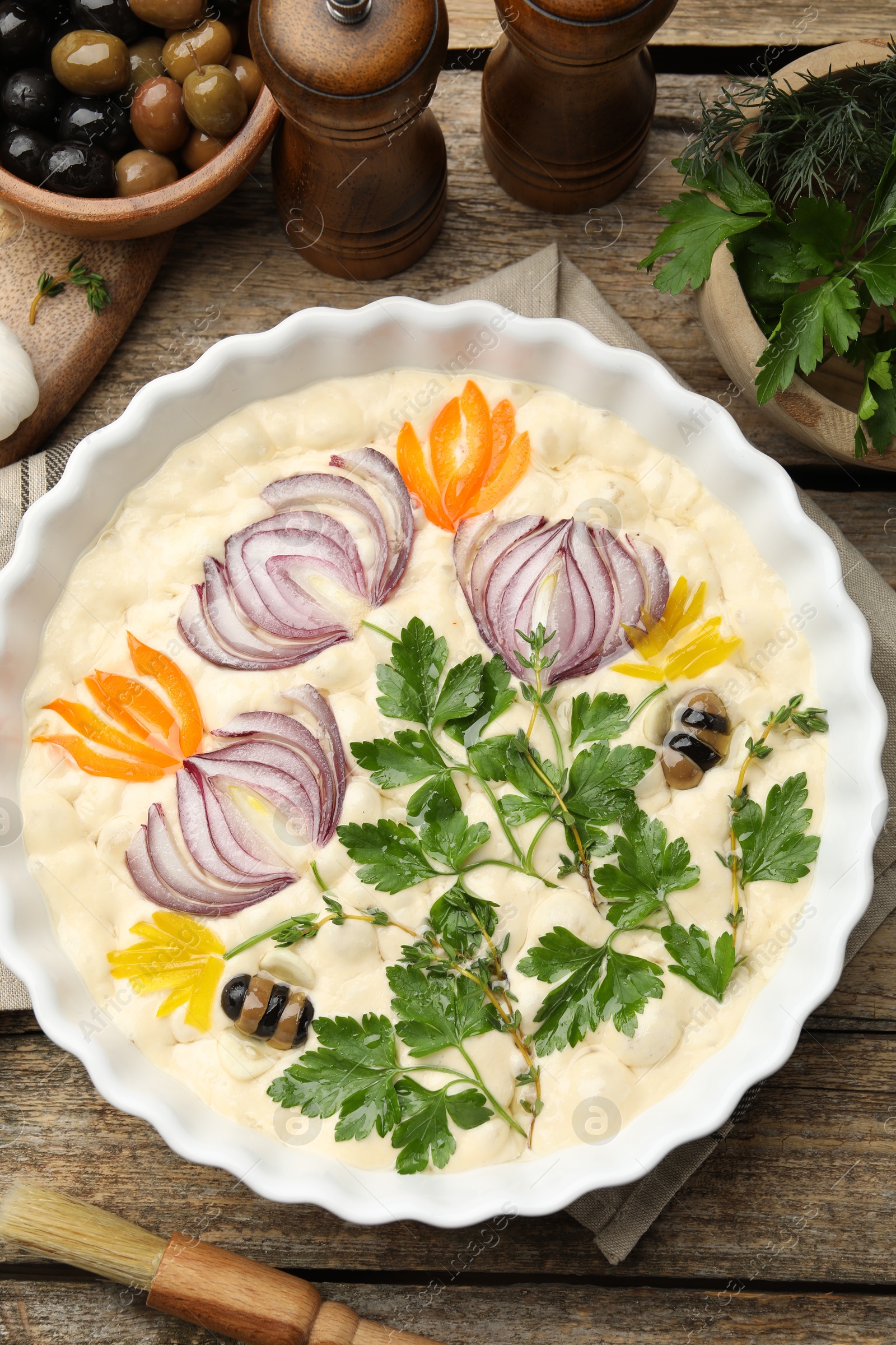 Raw focaccia with vegetables, olives, spices and brush on wooden table, flat lay Photo of Raw focaccia with vegetables, olives, spices and brush on wooden table, flat lay
