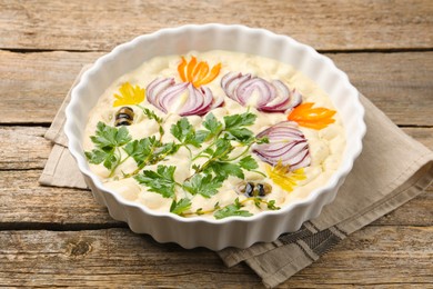 Photo of Raw focaccia with vegetables and olives in baking dish on wooden table, closeup