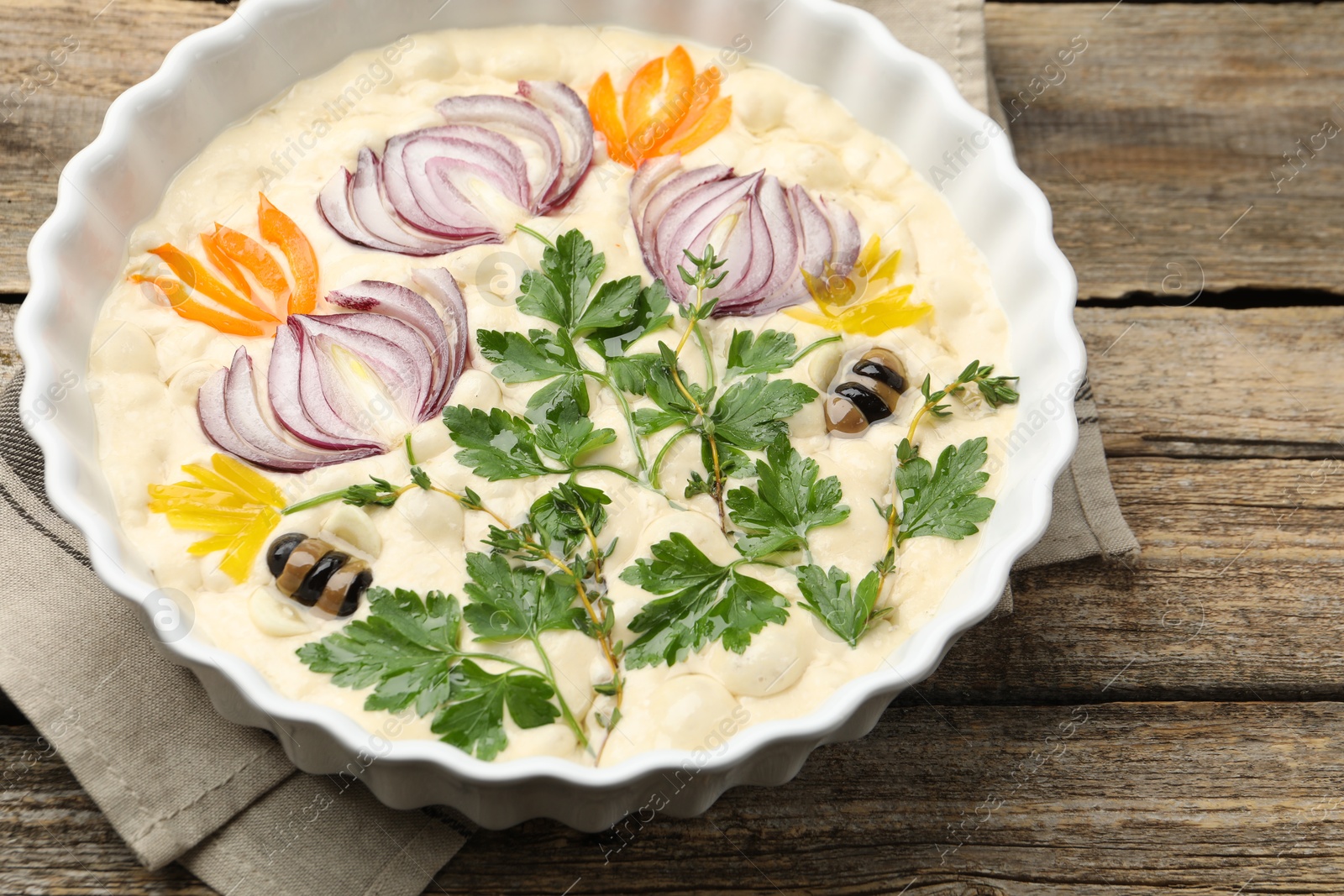 Raw focaccia with vegetables and olives in baking dish on wooden table, closeup Photo of Raw focaccia with vegetables and olives in baking dish on wooden table, closeup