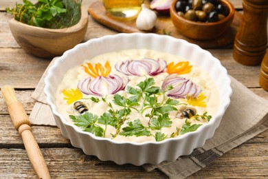 Photo of Raw focaccia with vegetables, olives, spices and brush on wooden table, closeup