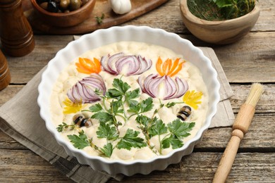 Photo of Raw focaccia with vegetables, olives, spices and brush on wooden table, closeup