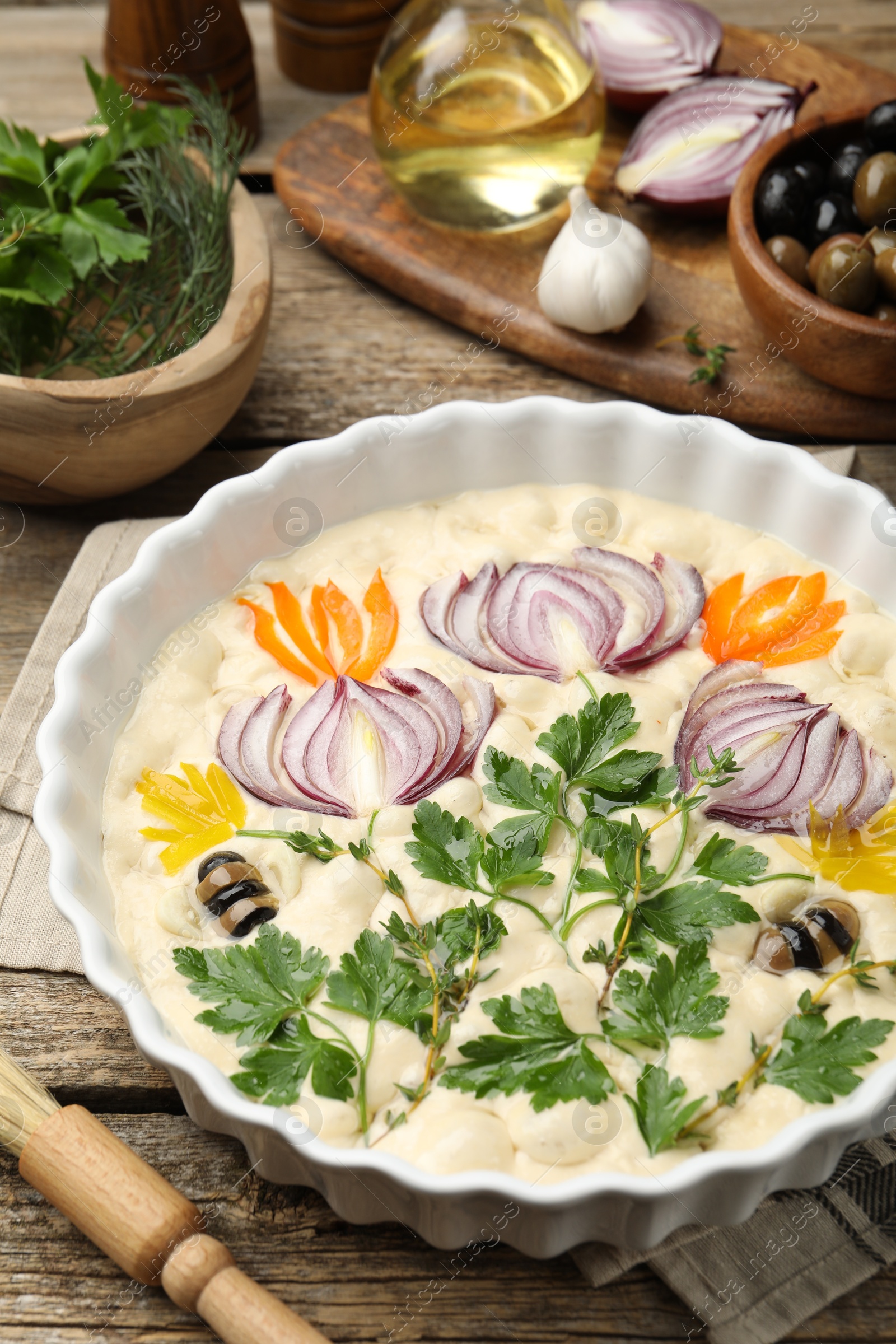 Raw focaccia with vegetables, olives, spices and brush on wooden table, closeup Photo of Raw focaccia with vegetables, olives, spices and brush on wooden table, closeup
