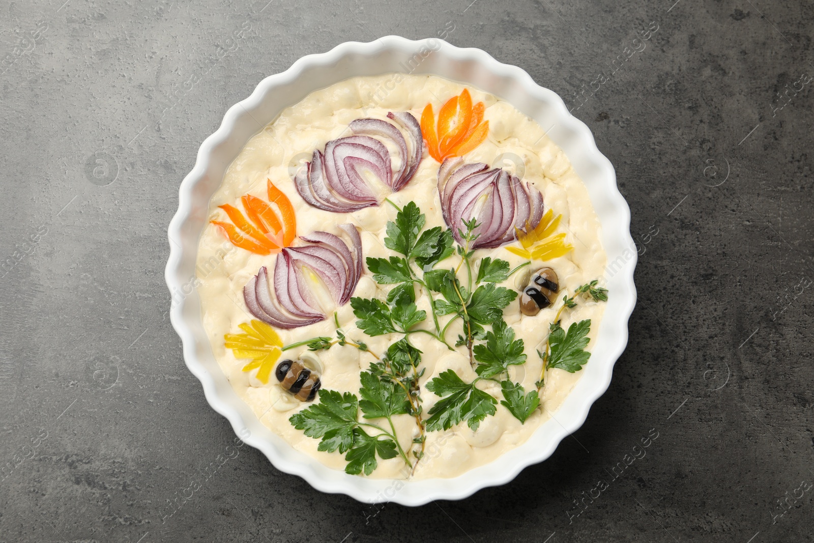 Raw focaccia with vegetables and olives in baking dish on grey table, top view Photo of Raw focaccia with vegetables and olives in baking dish on grey table, top view