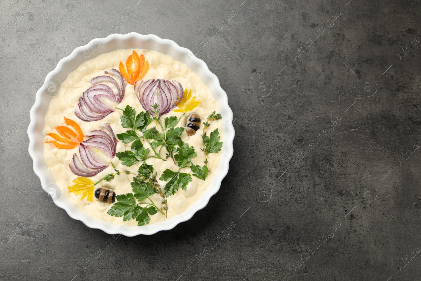Raw focaccia with vegetables and olives in baking dish on grey table, top view. Space for text Photo of Raw focaccia with vegetables and olives in baking dish on grey table, top view. Space for text