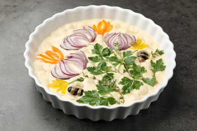 Photo of Raw focaccia with vegetables and olives in baking dish on grey table, closeup