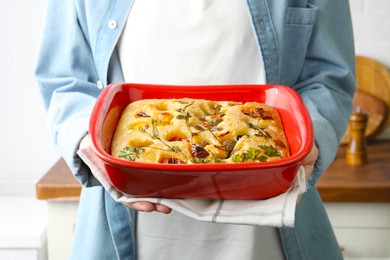 Photo of Woman holding delicious focaccia with vegetables and olives in kitchen, closeup
