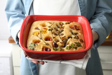 Photo of Woman holding delicious focaccia with vegetables and olives in kitchen, closeup