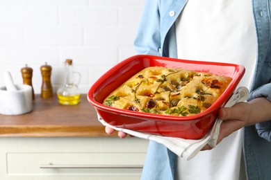 Photo of Woman holding delicious focaccia with vegetables and olives in kitchen, closeup