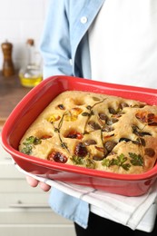 Photo of Woman holding delicious focaccia with vegetables and olives in kitchen, closeup
