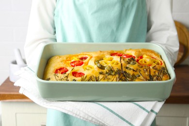 Photo of Woman holding delicious focaccia with vegetables and olives in kitchen, closeup