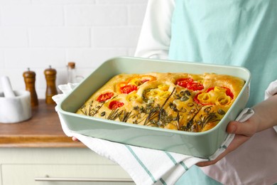 Photo of Woman holding delicious focaccia with vegetables and olives in kitchen, closeup