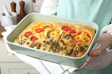 Photo of Woman holding delicious focaccia with vegetables and olives in kitchen, closeup