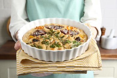 Photo of Woman holding delicious focaccia with vegetables and olives in kitchen, closeup