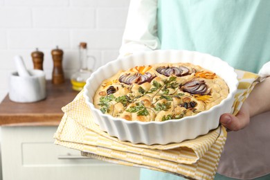 Photo of Woman holding delicious focaccia with vegetables and olives in kitchen, closeup