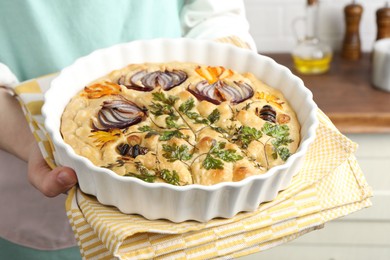 Photo of Woman holding delicious focaccia with vegetables and olives in kitchen, closeup