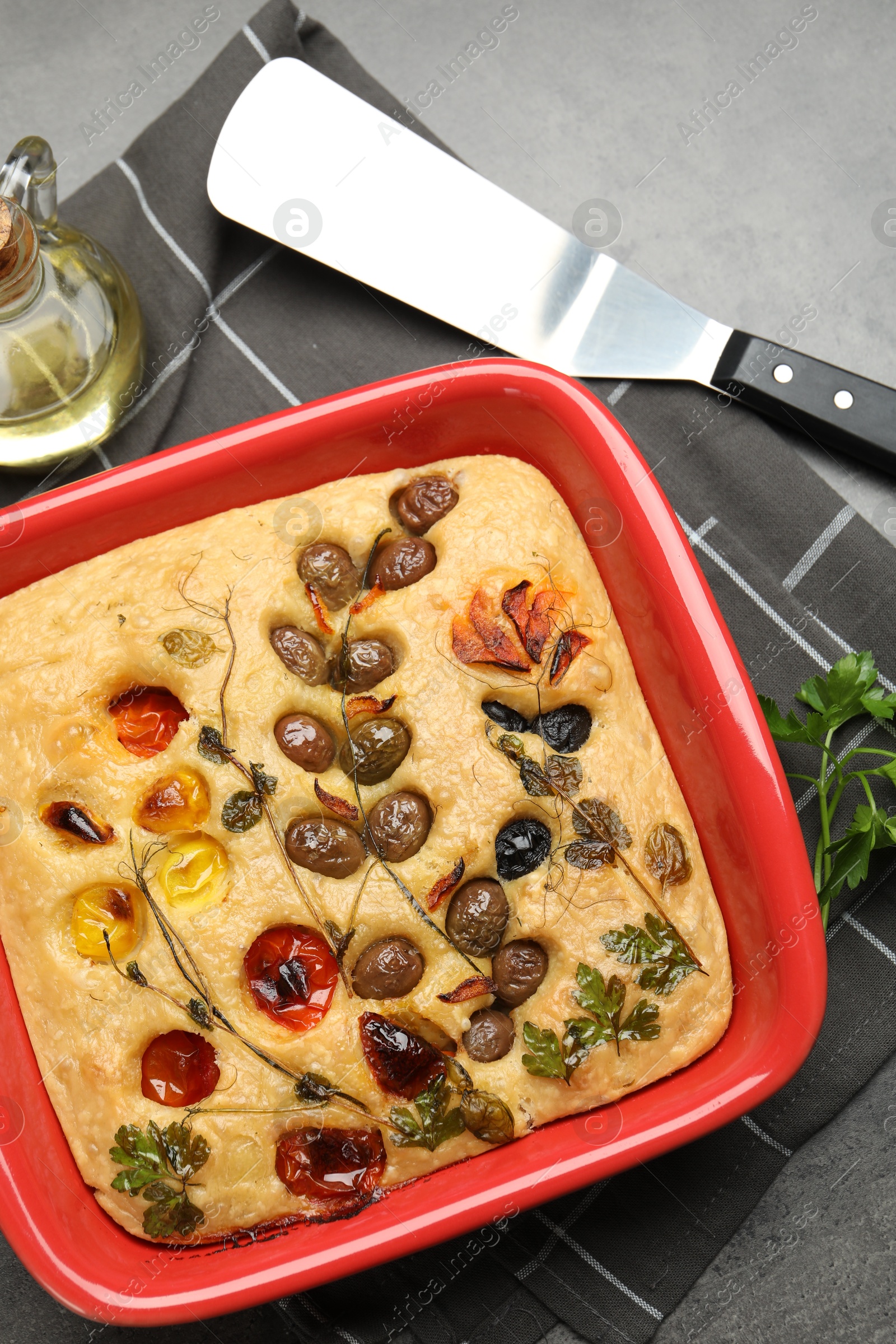 Delicious focaccia with vegetables, olives, spices and server on grey table, flat lay Photo of Delicious focaccia with vegetables, olives, spices and server on grey table, flat lay