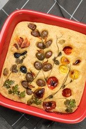 Photo of Delicious focaccia with vegetables and olives in baking dish on table, top view