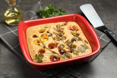 Photo of Delicious focaccia with vegetables, olives, spices and server on grey table, closeup