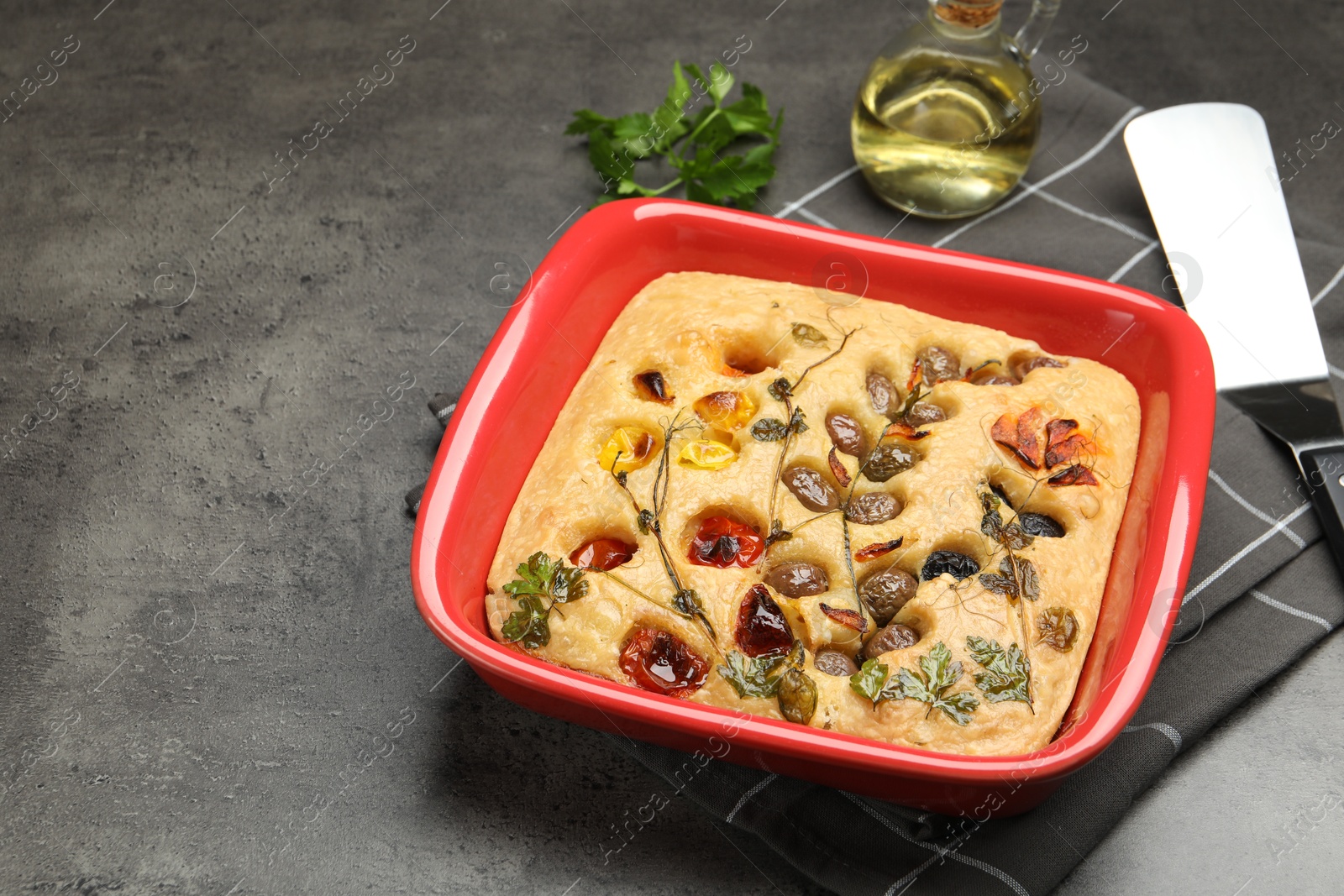 Delicious focaccia with vegetables, olives, spices and server on grey table, closeup. Space for text Photo of Delicious focaccia with vegetables, olives, spices and server on grey table, closeup. Space for text