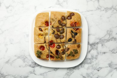 Photo of Cut delicious focaccia with flowers made of vegetables on white marble table, top view