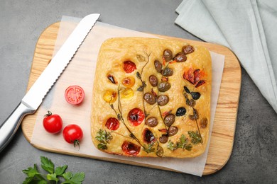 Photo of Delicious focaccia with flowers made of vegetables and knife on grey table, flat lay