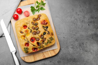 Photo of Delicious focaccia with flowers made of vegetables and knife on grey table, flat lay. Space for text
