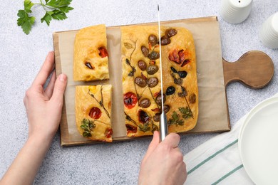 Photo of Woman cutting delicious focaccia at light grey table, top view