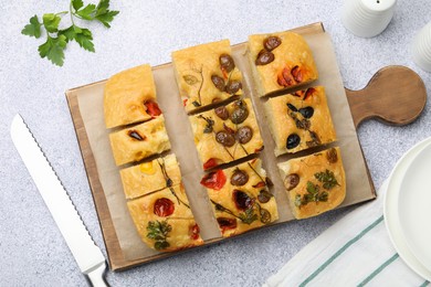 Photo of Cut delicious focaccia with flowers made of vegetables and knife on light grey table, flat lay