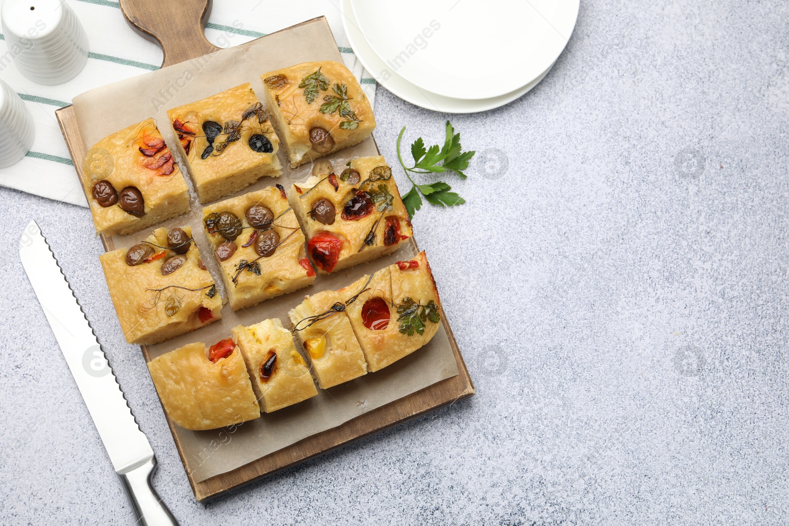 Cut delicious focaccia with flowers made of vegetables and knife on light grey table, flat lay. Space for text Photo of Cut delicious focaccia with flowers made of vegetables and knife on light grey table, flat lay. Space for text