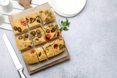 Photo of Cut delicious focaccia with flowers made of vegetables and knife on light grey table, flat lay. Space for text
