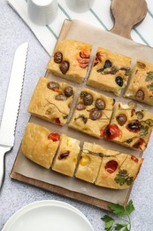 Photo of Cut delicious focaccia with flowers made of vegetables and knife on light grey table, flat lay