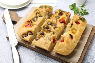 Photo of Cut delicious focaccia with flowers made of vegetables and knife on light grey table, closeup
