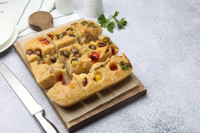 Photo of Cut delicious focaccia with flowers made of vegetables and knife on light grey table