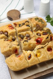 Photo of Cut delicious focaccia with flowers made of vegetables on light grey table, closeup