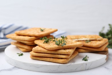 Photo of Tasty salty crackers with thyme on white marble table, closeup
