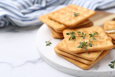 Photo of Tasty salty crackers with thyme on white marble table, closeup. Space for text