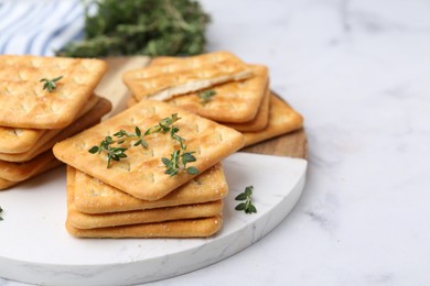 Photo of Tasty salty crackers with thyme on white marble table, closeup